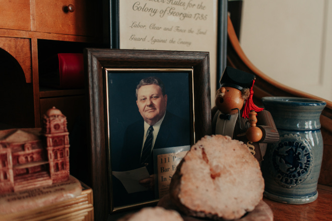 a framed picture of shannon's father on a desk, surrounded by trinkets.